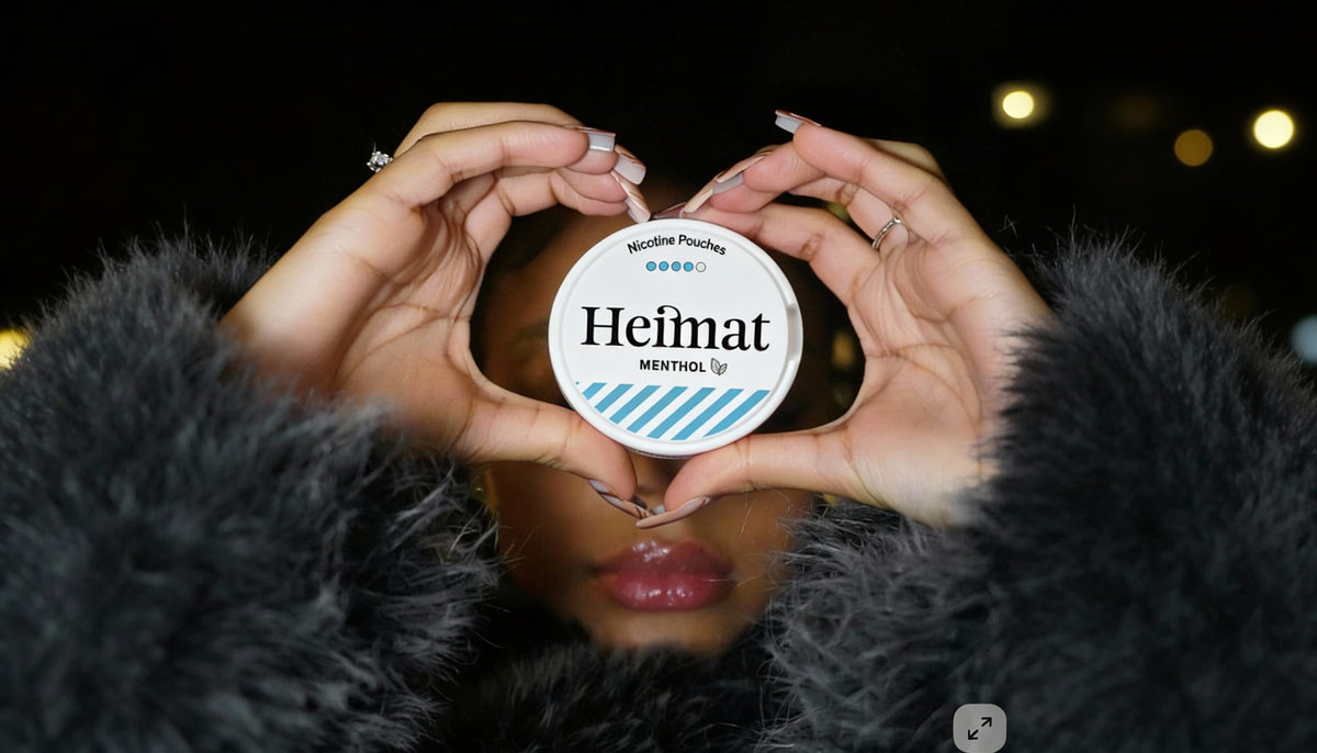 Dóza nikotínových vrecúšok Heimat Menthol v rukách zložených do srdca, lifestylový záber so ženou v čiernom kabáte