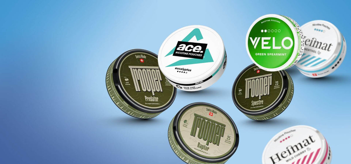 Výber snusu a nikotínových vrecúšok: dózy VELO Green Spearmint a Heimat na modrom pozadí